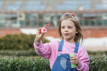 Cute happy girl playing with soap bubbles on a summer day. A child in the fresh air, in nature. The concept of a happy childhood and a holiday.