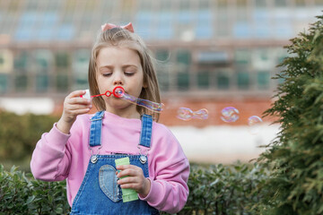 Cute happy girl playing with soap bubbles on a summer day. A child in the fresh air, in nature. The concept of a happy childhood and a holiday.