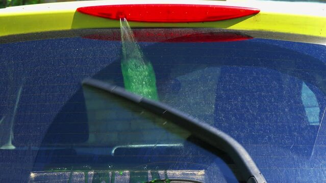 Closeup of clean water squirting onto a car&rsquo;s dirty rear windscreen or windshield, with the wiper arm activated.