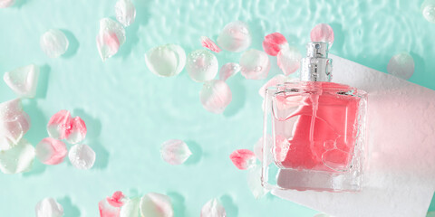 Perfume fragrance bottle on floral background. Top view of Transparent glass pink perfume bottle over rippled blue water background. splash of water. Flat lay, copy space