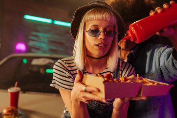 Stylish girls using ketchup with fast food outdoors.