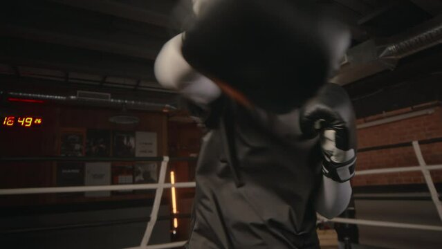 POV of determined young Muslim woman in black hijab and gloves looking at camera while boxing in boxing ring