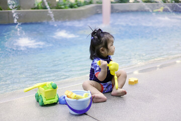 Asian baby girl playing with water toys by the pool. Little girl playing in outdoor swimming pool on summer vacation on luxury resort. Water toy for kids
