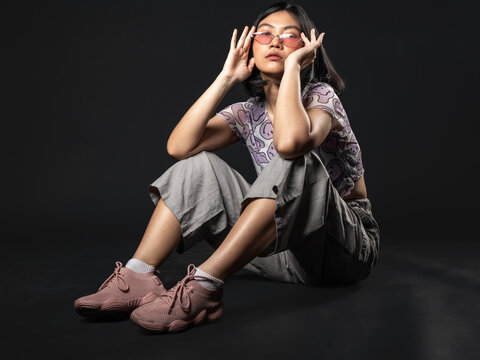 A portrait of a casual fashion style Asian Girl  sitting looking cool while posing with a Hip hop style. Isolated on a black background.