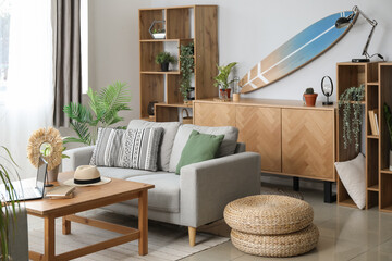 Interior of light living room with surfboard, table and sofa