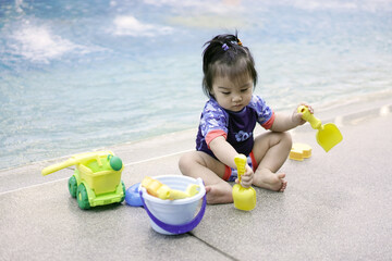 Asian baby girl playing with water toys by the pool. Little girl playing in outdoor swimming pool on summer vacation on luxury resort. Water toy for kids