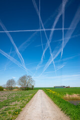 Country road below a sky full of vapor trails