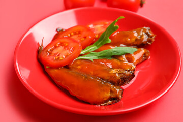 Plate with canned fish in sauce, arugula and tomatoes on red background