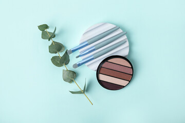 Decorative plaster podium with set of brushes, eyeshadows and eucalyptus branch on turquoise background