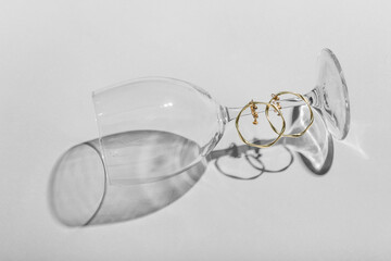 Fototapeta na wymiar Glass with golden earrings on light background