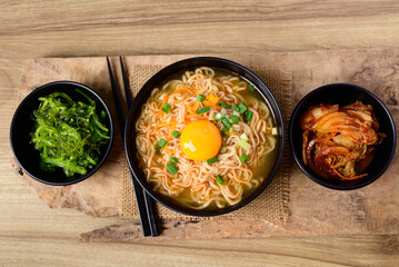 Asian instant noodle soup with fresh egg yolk eating with kimchi cabbage and seaweed salad, Table top view