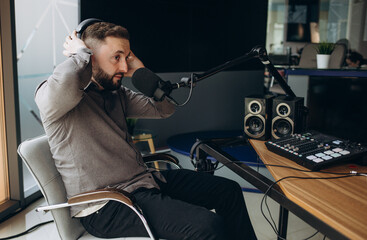 Handsome young latin man working as radio host at radio station sitting in front of microphone holding clipboard and using mobile phone.