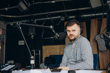 Portrait of smiling hispanic male radio presenter with clipboard hosting a show at radio station