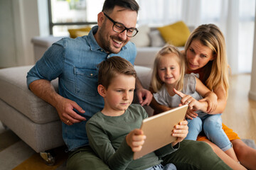 Happy young family having fun time at home. Parents with children using digital device.