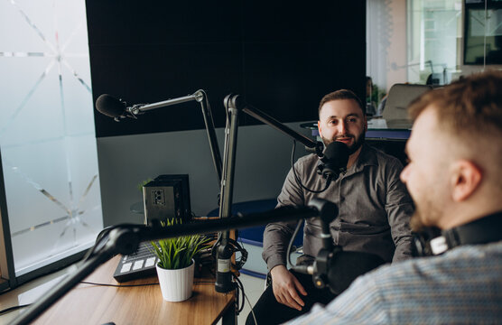 Two college podcasters laughing and having a good time in a studio. Two happy young men co-hosting a live audio broadcast.