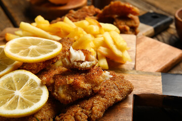Board of tasty fried codfish with lemon on wooden background, closeup