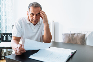 middle-aged man at table at home reading bill or letter