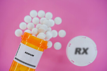 Sodium Rx medicine pills in plactic vial with tablets. Pills spilling   from yellow container on pink background.