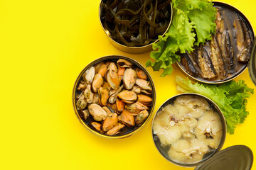 Opened tin cans with different seafood on yellow background
