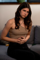 Brunette girl has abdominal pain. Young woman touching her belly with upset face expression