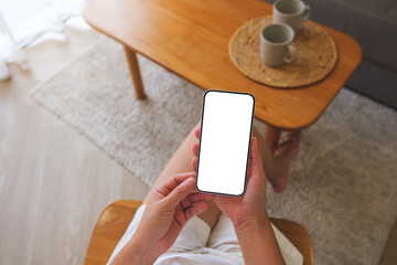 Top view mockup image of a woman holding and using mobile phone with blank desktop white screen at...