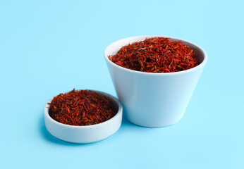 Bowls with pile of saffron on blue background