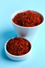 Bowls with pile of saffron on blue background