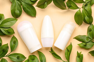 Different deodorant bottles and leaves on yellow background