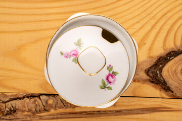 One old porcelain sugar bowl on a wooden table, macro, top view.