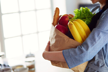 Young woman holding grocery shopping bag with vegetables .Standing in the kitchen. - 596619354