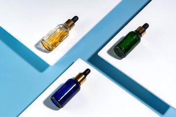 Face serum dropp bottles on white podiums on blue background. Home routine skin care cosmetic set. Unbranded bottles for your design.