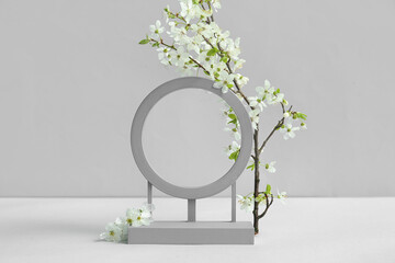 Decorative podium and blooming branch on grey background
