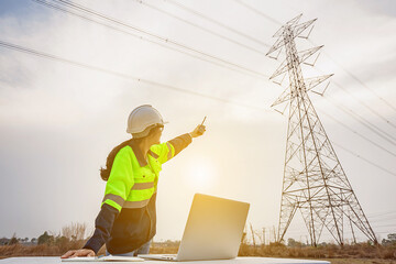 Asian female electrical engineer working inspecting power station near high voltage pylons with...