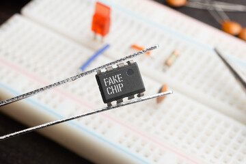 Fake chip concept: An integrated circuit held with tweezers on top of a breadboard populated with...