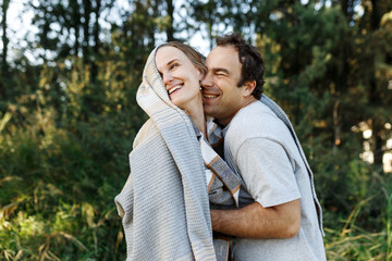 Fototapeta premium Romantic affectionate couple on a holiday. Man and woman standing together in balcony wrapped in blanket. Couple embracing and smiling
