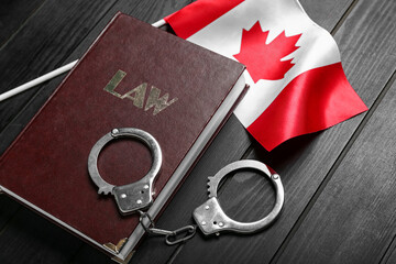 Canadian flag with law book and handcuffs on dark wooden background, closeup