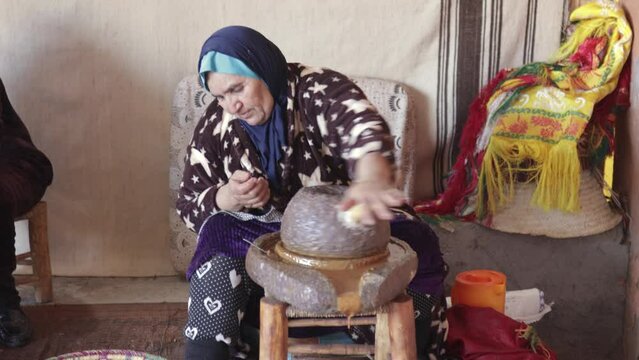 Arab senior woman sitting in cooperative working grinding argan nuts to extract oil
