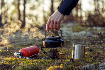 A man removes a boiling kettle from a multi fuel stove in the forest.