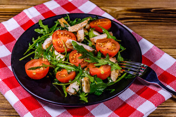 Roasted chicken breasts and salad with arugula and cherry tomatoes in a black plate