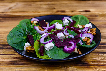 Salad with spinach leaves, feta cheese, beetroot, walnuts and onion on a black plate