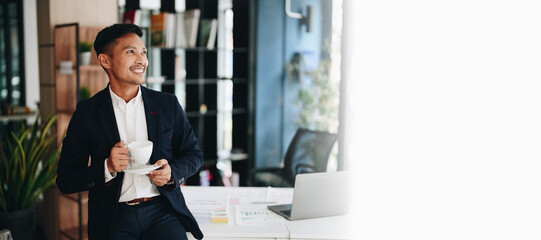 Portrait of an Asian male business owner standing with a computer showing happiness after a successful investment