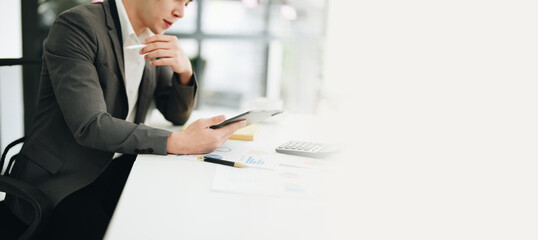 Portrait of a young Asian woman showing a smiling face as she uses his phone, computer and financial documents on her desk in the early morning hours
