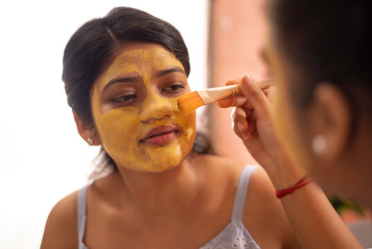 Woman applying turmeric face pack on her friend's face