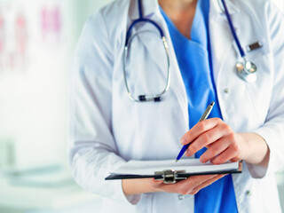 Doctor with a stethoscope, holding a notebook in his hand. Close-up of a female doctor filling up medical form at clipboard while standing straight in hospitalDoctor with a stethoscope, holding a note