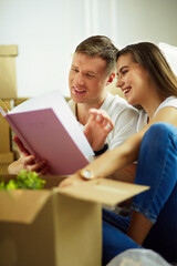 Young couple holding album while sitting on floor in new house.