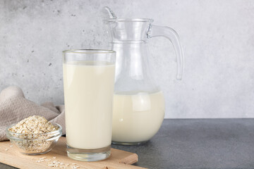 A jug and a glass of oat milk, oatmeal on a gray background. The concept of alternative lactose-free dairy products.