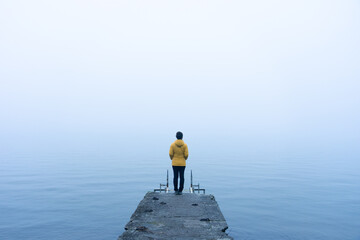 Woman with a yellow jacket looking at the horizon on a pier on a very foggy day at Lake Sanabria. Zamora, Spain.