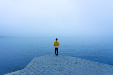 Woman with a yellow jacket looking at the horizon on a pier on a very foggy day at Lake Sanabria. Zamora, Spain.