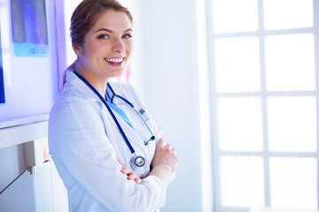 Young woman medic in white uniform standing in clinic's office.