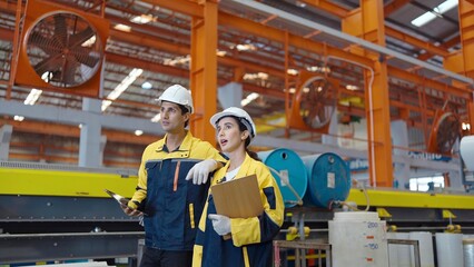 Two manufacturing employees in hard hats walk in steel metal manufacturing factory plant industry
